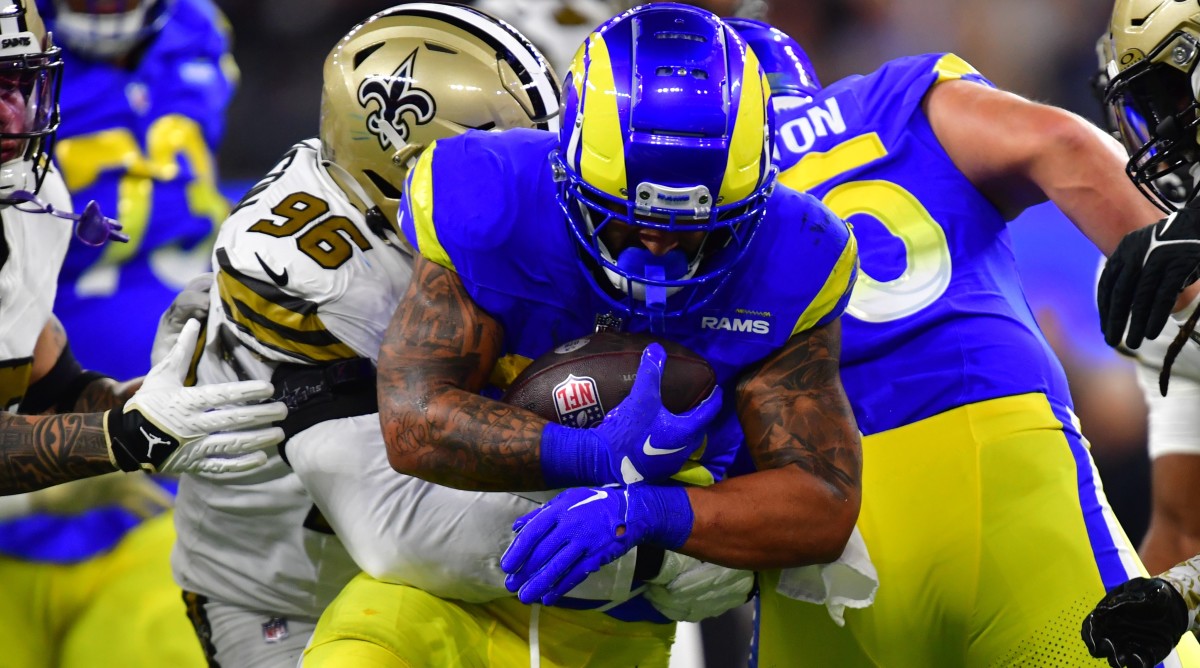 Los Angeles Rams running back Kyren Williams carries the football with a Saints defender draped around him.
