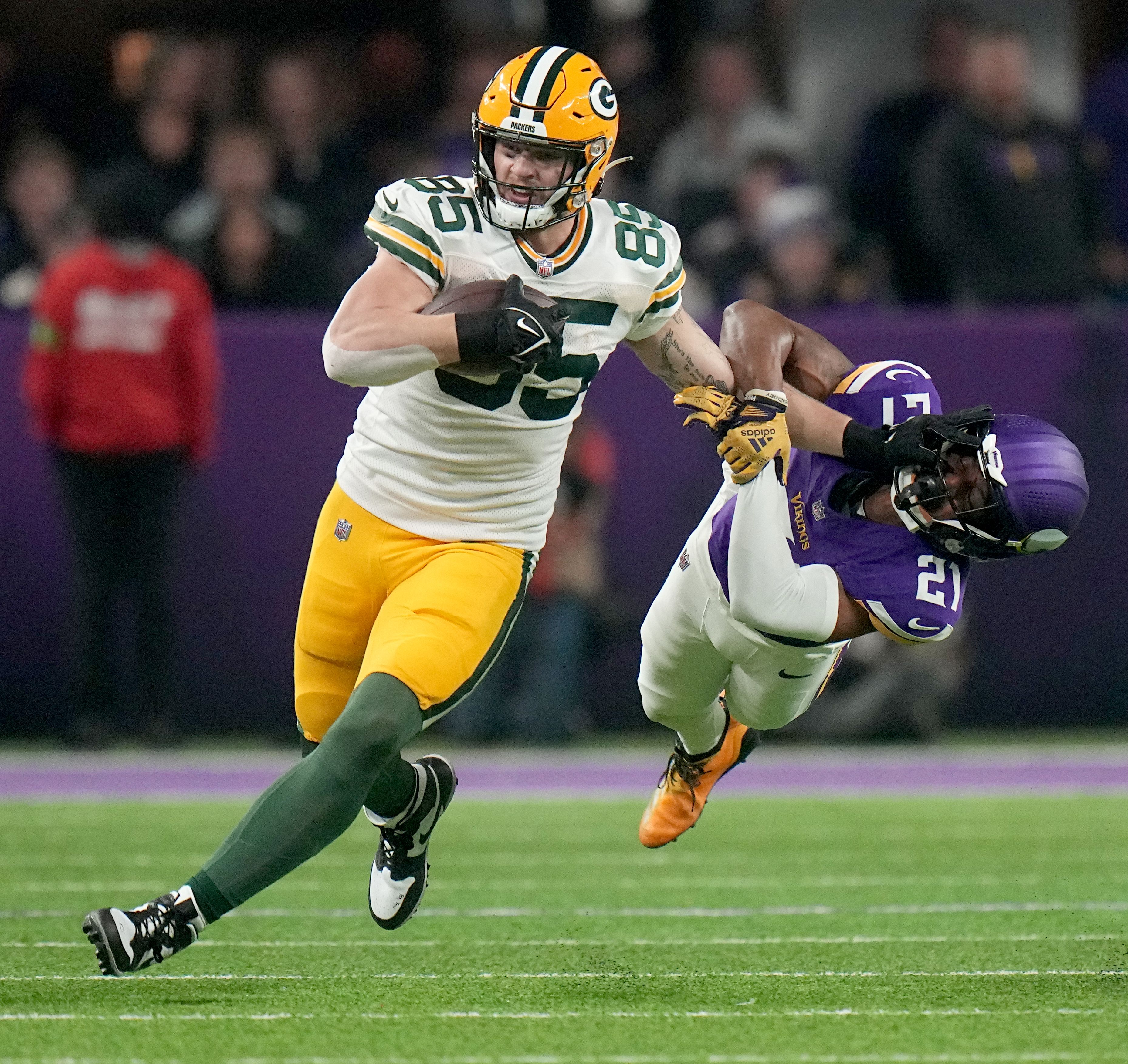Tucker Kraft catches a pass and stiff-arms a Vikings defender to the turf.