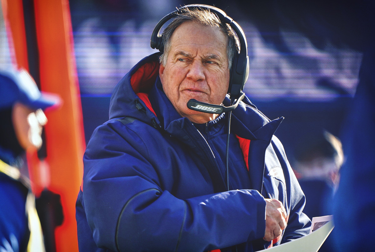 Bill Belichick looks over his shoulder wearing a headset and a winter coat