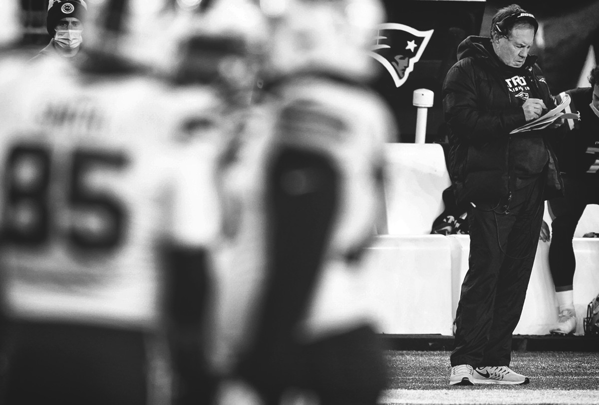 Bill Belichick stands writing on a clipboard in the background of a group of Patriots players