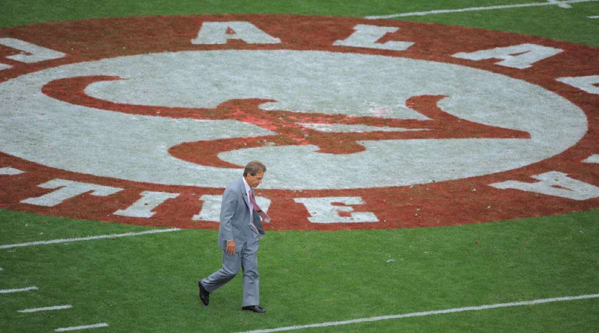 An overhead shot of Nick Saban walking near midfield with the Alabama midfield logo in the background.