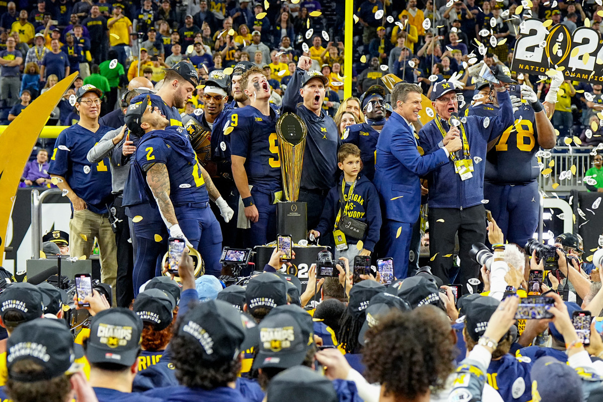 Jim Harbaugh, his father and Michigan players celebrate on stage with the trophy after winning the national championship.