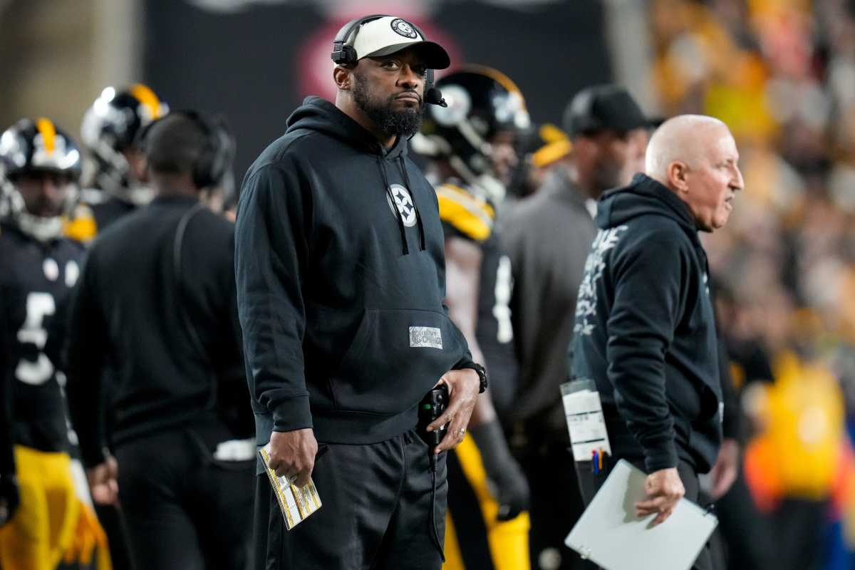 Mike Tomlin stands on the sideline with one hand on his waistband as the other holds a paper
