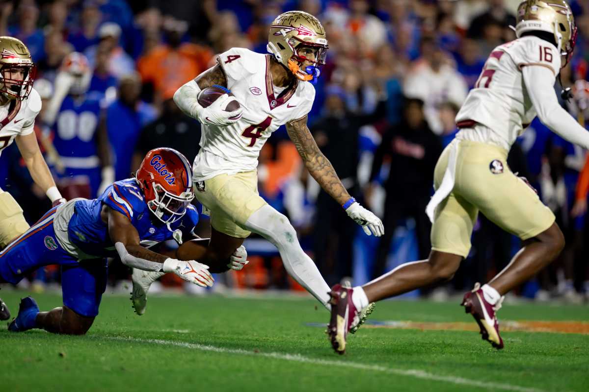 keon coleman runs with the ball in one hand as a Florida defender tries to grab his leg