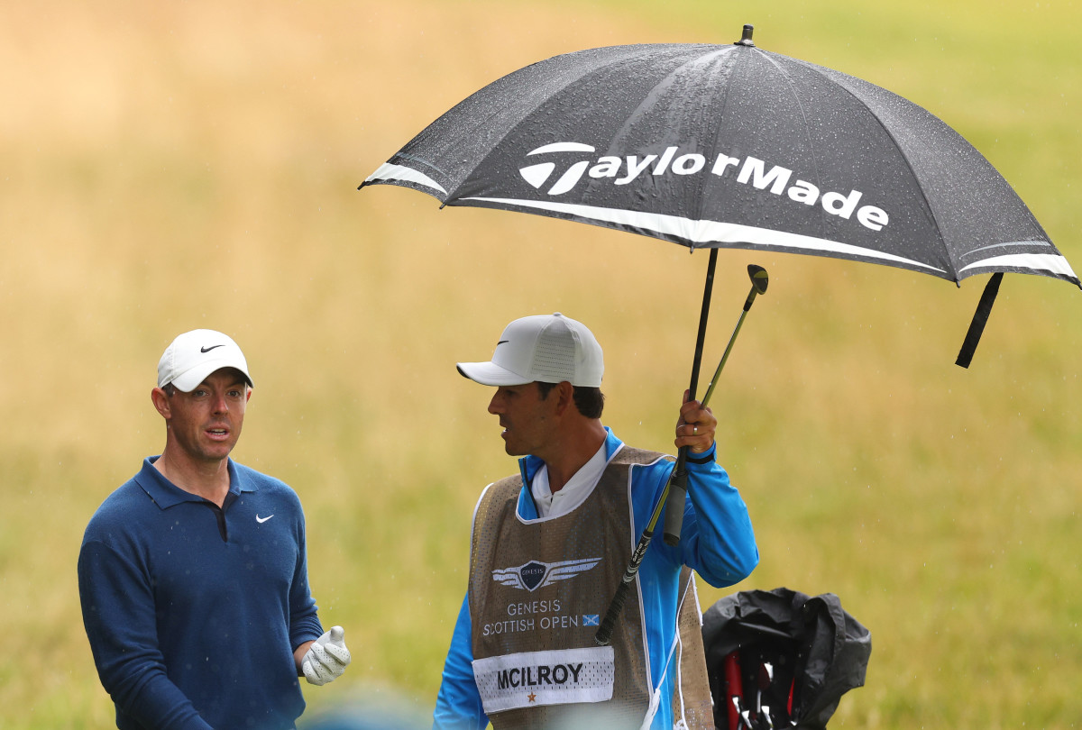Rory McIlroy of Northern Ireland and his caddie Harry Diamond shelter from the rain under an umbrella as they wait for a ruling on the 18th green during Day Two of the Genesis Scottish Open at The Renaissance Club on July 14, 2023 in United Kingdom.