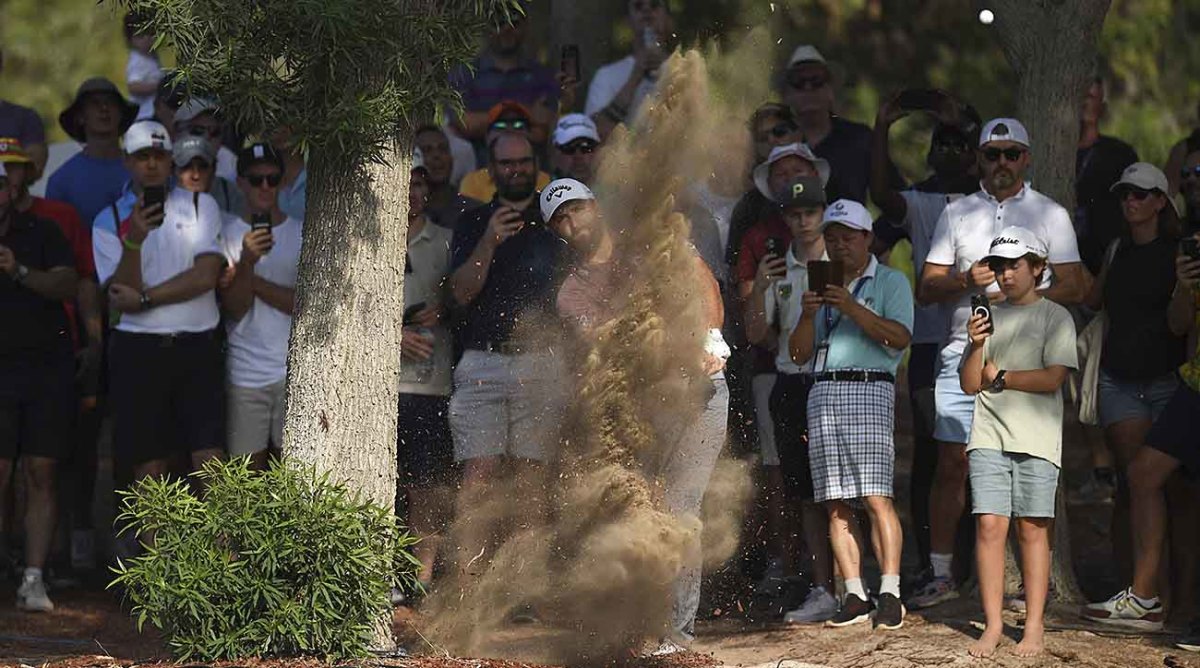 Jon Rahm hits a shot from off the fairway and kicks up a cloud of dirt at the 2022 DP World Tour Championship.