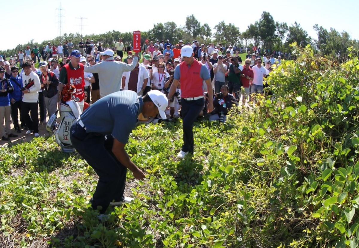 Tiger Woods inspects his ball as Martin Kaymer moves closer to help during the 2013 Abu Dhabi HSBC Golf Championship. Woods mistakenly took relief, incurred a 2-stroke penalty and missed the cut.