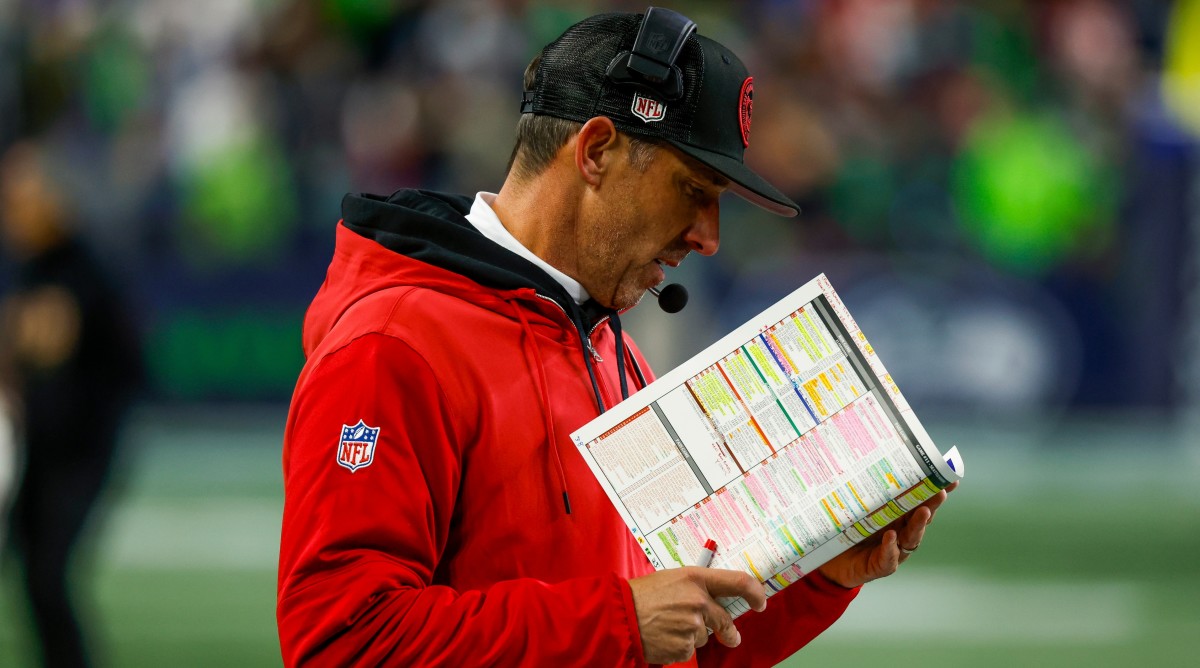 San Francisco 49ers head coach Kyle Shanahan stands on the sideline, reading from his playsheet during a game.