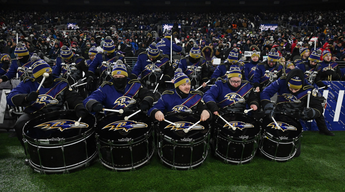 Members of the Marching Ravens marching band sit on the sidelines ahead of a halftime performance
