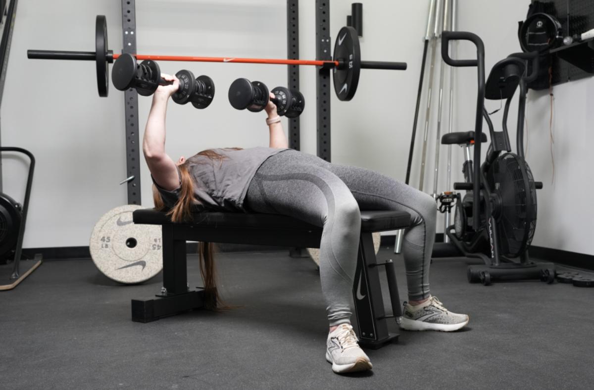 woman lying faceup on nike rolling weight bench performing chest press with dumbbells