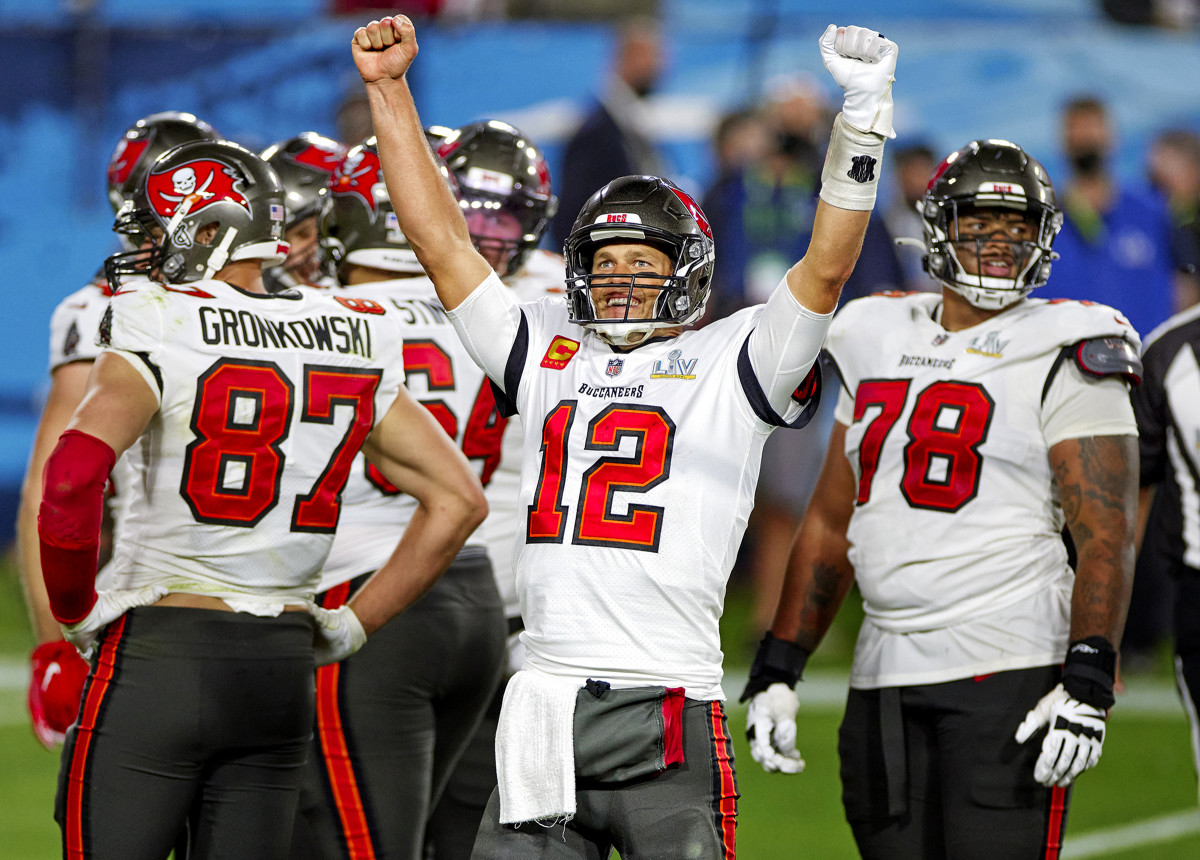 Tom Brady puts his hands up in the air while other Bucs players stand around him