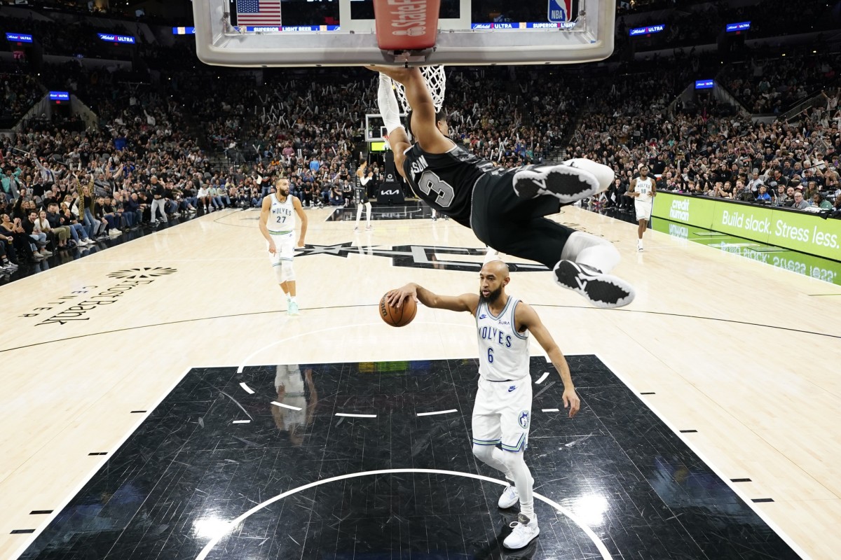 Jan 27, 2024; San Antonio, Texas, USA; San Antonio Spurs forward Keldon Johnson (3) hangs from the rim after dunking over Minnesota Timberwolves guard Jordan McLaughlin (6) during the second half at Frost Bank Center.