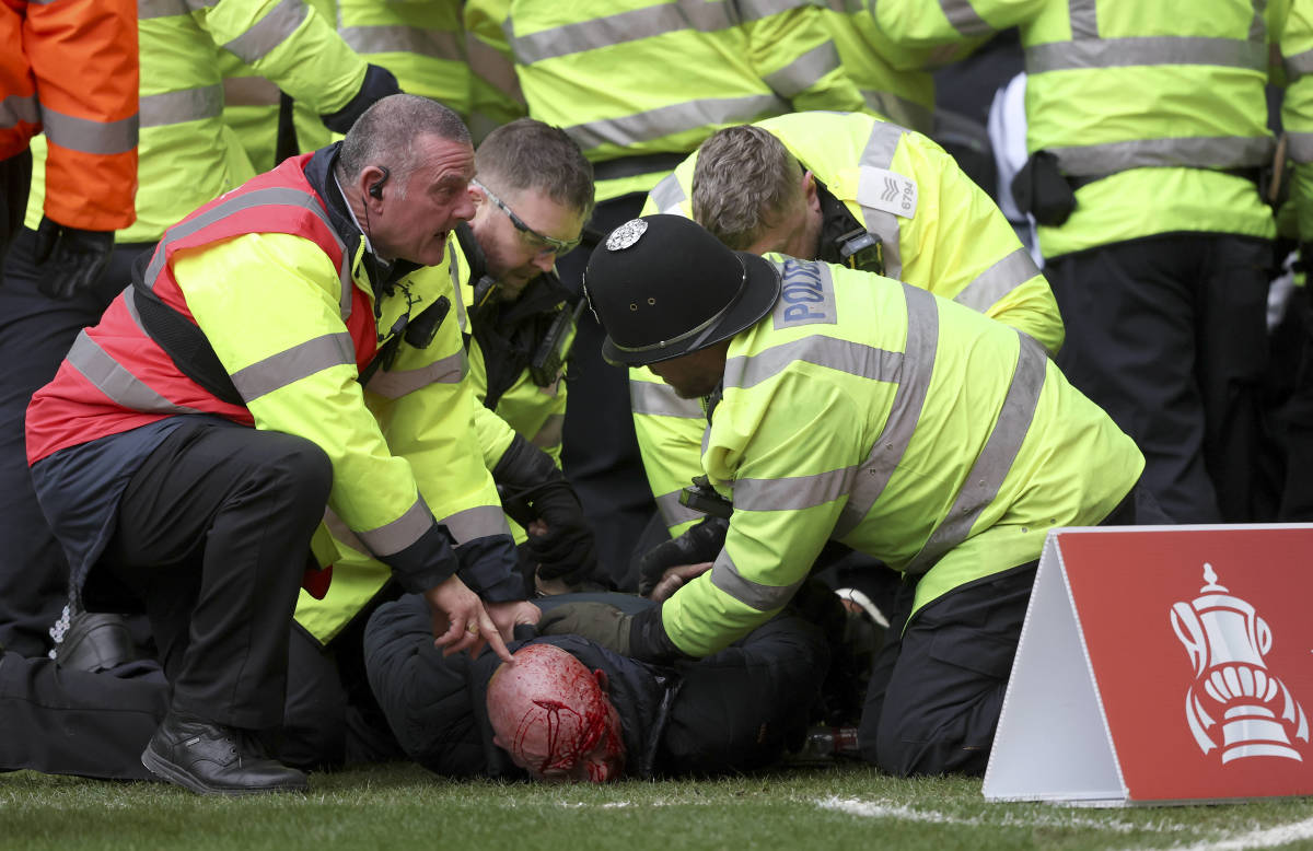 Police officers and a security steward pictured restraining an injured fan following crowd violence during an FA Cup game between West Brom and Wolves in January 2024