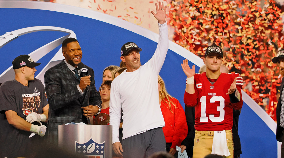 Christian McCaffrey, Michael Strahan, Kyle Shanahan and Brock Purdy all stand on stage celebrating as confetti falls around them