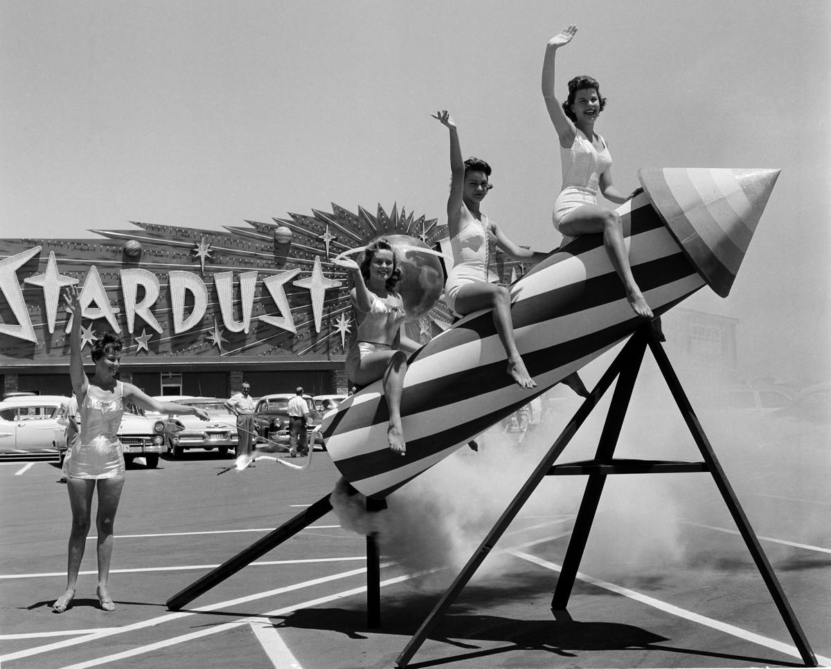 A black-and-white photo of three women sitting on a rocket outside of the Stardust casino in Las Vegas.